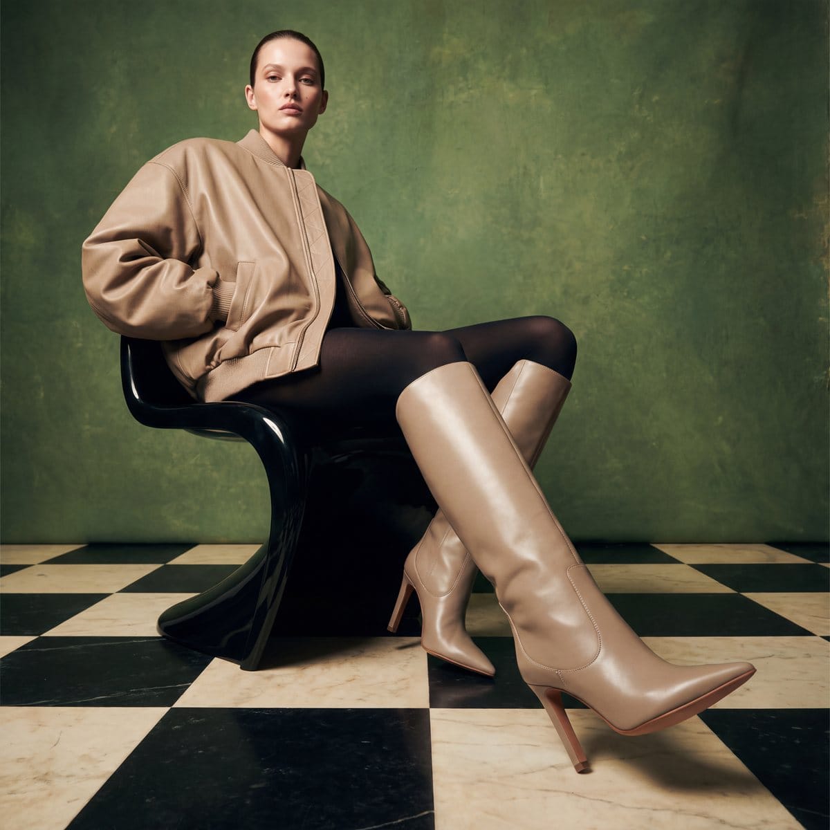 Model in beige knee-high boots on a black chair